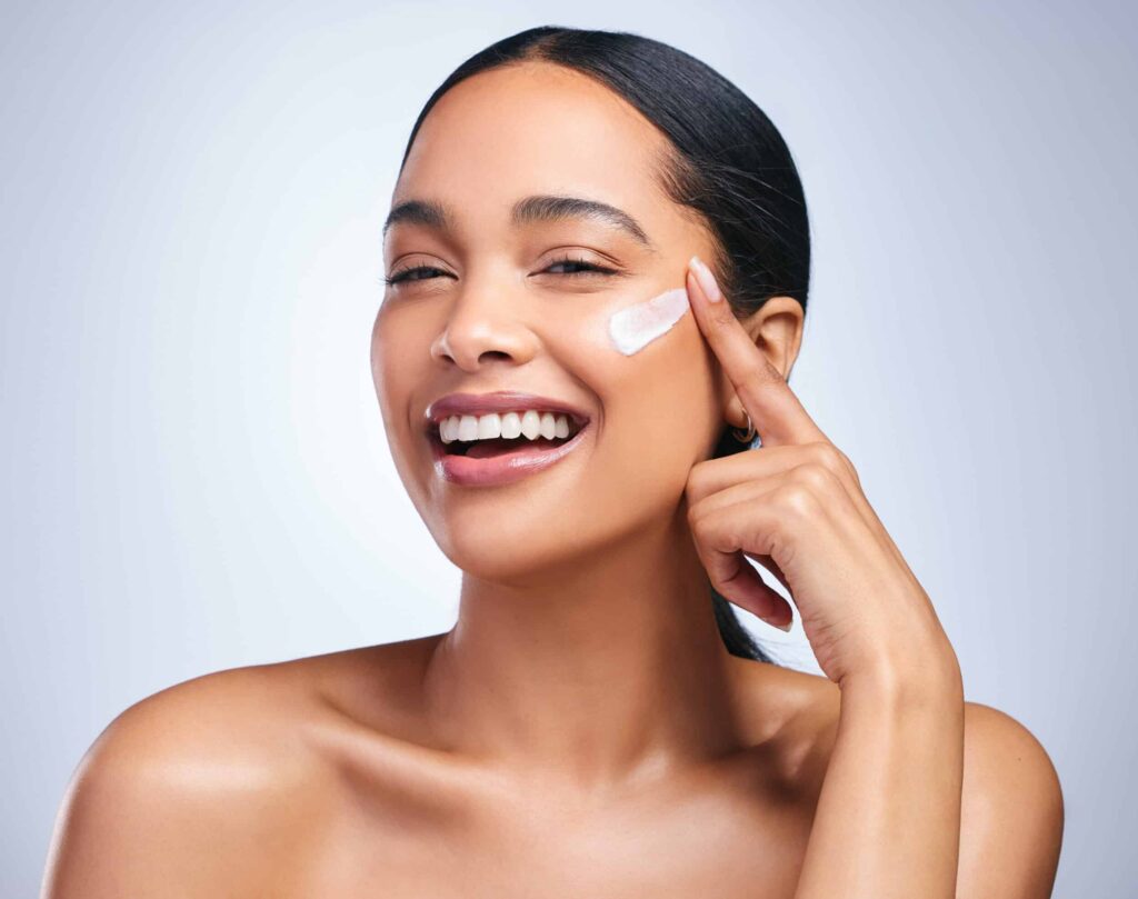 Portrait of an attractive young woman applying moisturiser against a grey background