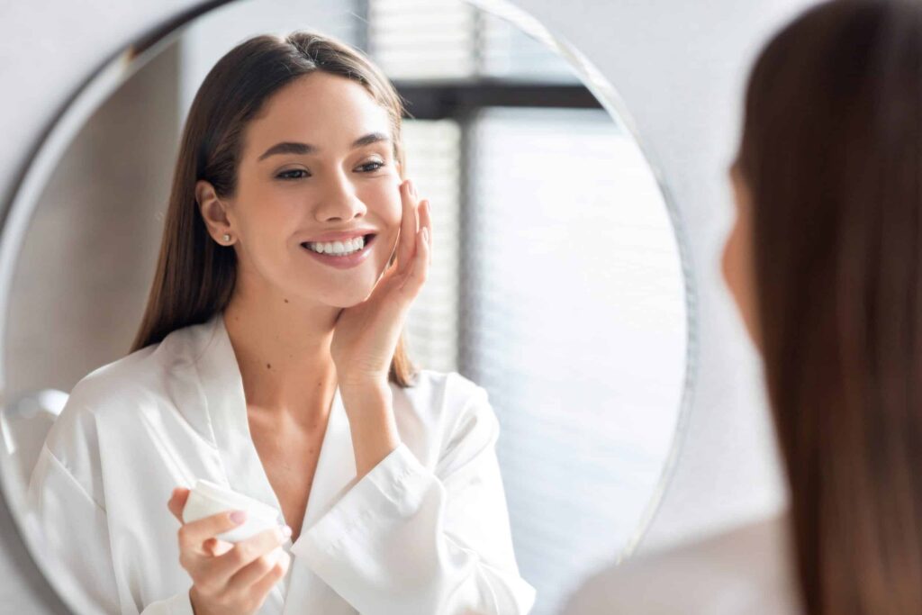 Woman smiling in the mirror at her smooth skin after a chemical peel in Ashburn, VA